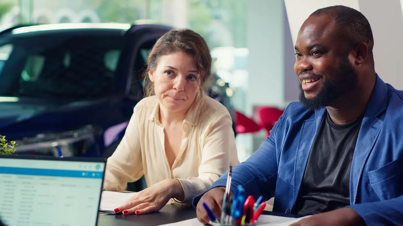 Two customers filling in a car loan application at a dealership desk