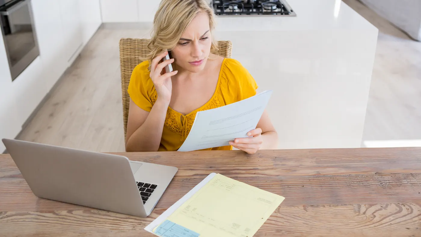 A woman on the phone reading a bill at her kitchen table